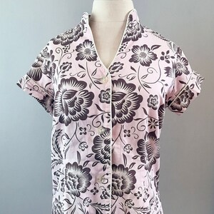 May include: A pink and brown floral print short-sleeved button-up shirt with a white collar and trim.