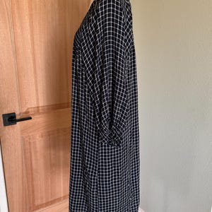 May include: A navy blue and white checkered dress with long sleeves. The dress is displayed on a mannequin and has a loose, flowing fit. The fabric has a grid pattern.