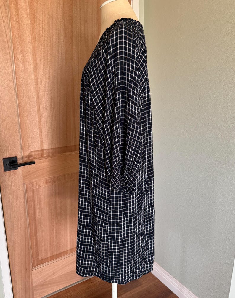 May include: A navy blue and white checkered dress with long sleeves. The dress is displayed on a mannequin and has a loose, flowing fit. The fabric has a grid pattern.