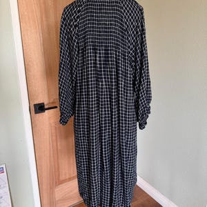 May include: A long, navy blue dress with a white grid pattern. The dress has long sleeves and a round neckline. The fabric appears to be lightweight and flowing, suitable for casual wear. The dress is displayed on a mannequin.