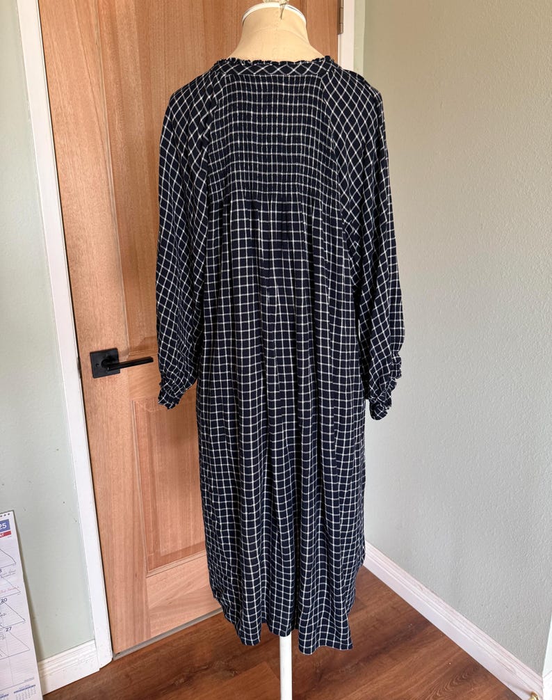 May include: A long, navy blue dress with a white grid pattern. The dress has long sleeves and a round neckline. The fabric appears to be lightweight and flowing, suitable for casual wear. The dress is displayed on a mannequin.
