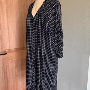 May include: A long-sleeved, knee-length dress in a navy blue and white grid pattern. The dress features a V-neckline, button-down front, and gathered detailing at the shoulders and cuffs. The dress is displayed on a mannequin.