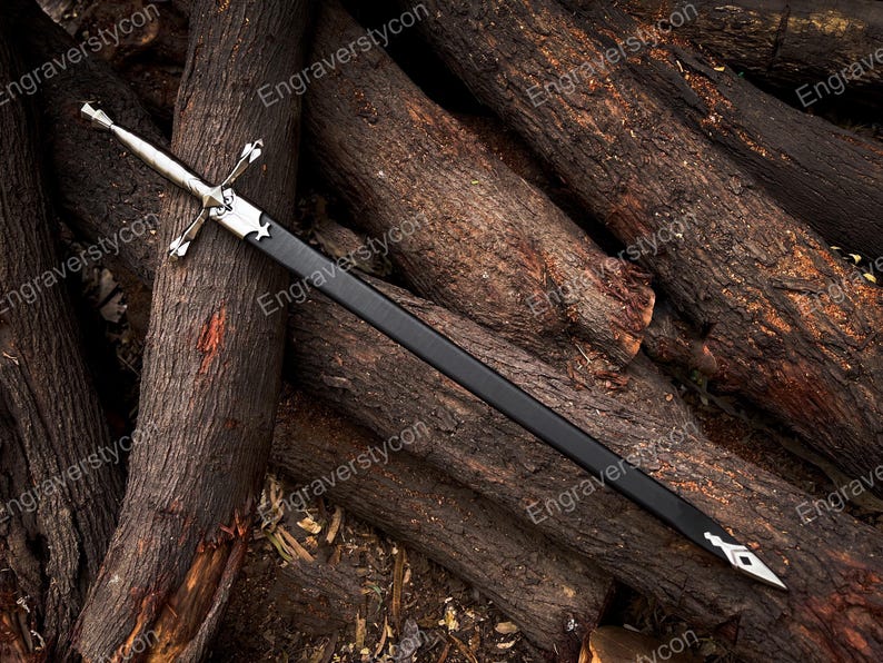 May include: A silver-toned metal sword with a cross-shaped guard and a black scabbard. The scabbard features a silver-colored metal fitting at the top near the hilt and a pointed silver-colored metal chape at the bottom tip of the blade casing.