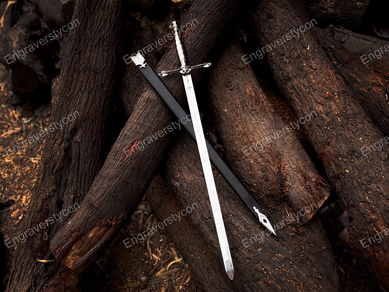 May include: A silver-toned metal sword with a detailed crossguard and pommel, positioned diagonally across a black scabbard. The scabbard features silver-colored metal fittings at the top and pointed tip, contrasting with the polished blade.