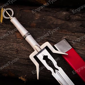 May include: A silver-toned sword with a white handle and a circular pommel, featuring a unique crossguard design with pointed extensions. The blade is partially visible next to a bright red scabbard with a metallic silver tip and throat.