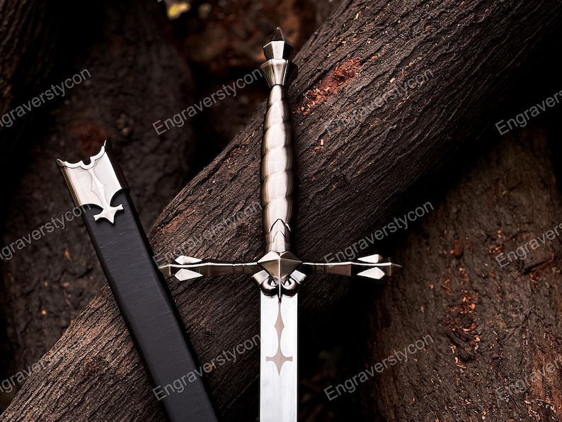 May include: A silver-toned metal sword featuring a ridged handle, a cross-shaped guard with pointed ends, and a blade with a decorative cutout near the hilt. A black scabbard with a silver metal throat piece is positioned alongside the sword.