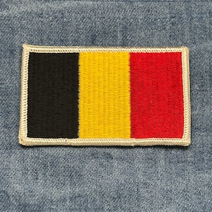 May include: Rectangular patch featuring the flag of Belgium. The flag design includes vertical stripes of black, yellow, and red. The patch has a white border and is set against a blue denim background.