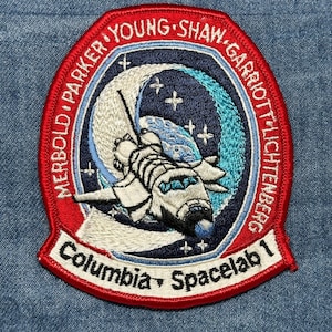 May include: Embroidered patch featuring the Columbia Spacelab 1 mission. The patch has a red border with the names of the astronauts. The central design includes a space shuttle, a crescent moon, and stars, with the text "Columbia Spacelab 1".