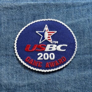 May include: A blue, circular patch with white stitching around the edge. The patch features a white star with red and white stripes, the text "USBC 200 GAME AWARD" in red and white.