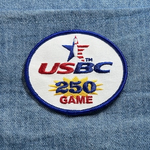 May include: An embroidered patch with a white oval center and a blue border. The patch features the text "USBC" in red and blue, a star and stripes graphic, and the text "250 GAME" in blue and gold.
