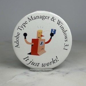 May include: White button with a retro computer graphic. The button features a cartoon robot with the text "Adobe Type Manager & Windows 3.1" and the phrase "It just works!" in a circular design. The robot is red, orange, and beige.