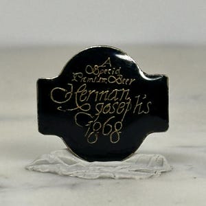 May include: A black metal sign with the words "A Special Premium Beer Herman Joseph's 1868" in gold script. The sign has a rounded top and a rectangular bottom. The sign is on a white surface.