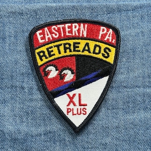 May include: A shield-shaped patch with the words "EASTERN PA. RETREADS" in white and yellow lettering. The patch features a red, black, and white design with two white birds. The bottom of the patch reads "XL PLUS" in red.