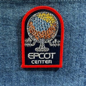 May include: Embroidered patch featuring the EPCOT Center logo. The patch has a navy blue background with a red border. The logo depicts a geodesic sphere in yellow, blue, and orange, with the words "EPCOT CENTER" in white.