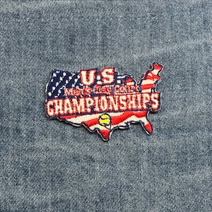 May include: Embroidered patch in the shape of the United States, featuring the text "U.S. Men's Clay Court Championships." The patch has a red, white, and blue color scheme, with a tennis ball graphic.