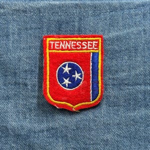 May include: A white ceramic mug with a black handle and the text "But First, Coffee" in a bold, black font. The mug is set against a blurred background, suggesting a cozy setting.