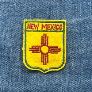 May include: Yellow patch with a green border and the words "NEW MEXICO" in red. The patch features a red and yellow Zia symbol. The patch is on a blue denim background.