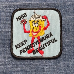 May include: Embroidered patch with a light blue background and a black border. The patch features a cartoon character with a yellow body, red arms and legs, and a smiling face. The text "1988" and "KEEP PENNSYLVANIA BEAUTIFUL" are also included.