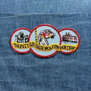May include: Embroidered patch with three circular designs on a blue denim background. The patch features a steamboat, a horse, and a building, with the text "88 Pittsburgh NCA Convention" in yellow.