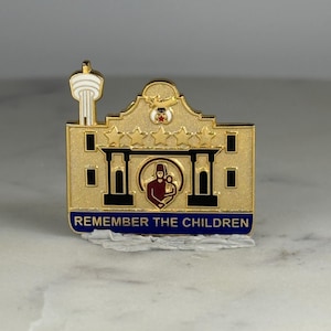 May include: A gold-colored pin in the shape of a building with a tower. The pin features a red and white figure inside a circle, with the text "REMEMBER THE CHILDREN" in blue.