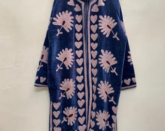 May include: A long, deep blue velvet coat featuring light pink embroidered floral motifs and a vertical border of repeating heart shapes along the front opening. The garment has long sleeves and a high collar, with dark red accents in the flower centers.