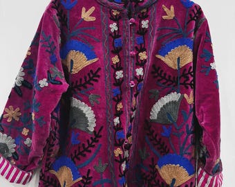 May include: A magenta velvet jacket with intricate floral embroidery in blue, gold, gray, and black. The jacket features a high collar, button closure, and striped cuffs. The design includes fan-shaped and leaf-like patterns.