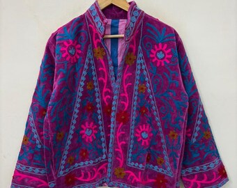 May include: A vibrant, embroidered jacket in shades of purple, pink, and teal. The jacket features intricate floral and geometric patterns. The jacket is hanging on a wooden hanger against a neutral background.