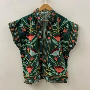 Puede incluir: Chaqueta de terciopelo verde oscuro con bordados florales coloridos. La chaqueta tiene cuello mandarín y forro a rayas. El bordado incluye flores y hojas rosas, amarillas y azules, creando un estilo bohemio.
