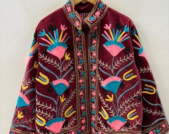 May include: A burgundy velvet jacket with colorful floral embroidery. The jacket features a mandarin collar and is adorned with pink, blue, yellow, and gold thread floral designs. The embroidery is detailed and covers the front and sleeves.