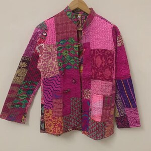 May include: A patchwork jacket in shades of pink, magenta, and purple. The jacket features a mandarin collar, long sleeves, and two front pockets. The fabric is a mix of patterned textiles, creating a unique, bohemian style.