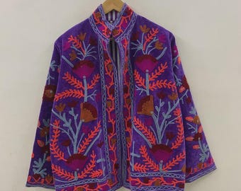 May include: A purple jacket with floral embroidery in shades of orange, pink, and blue. The jacket has a high collar and is hanging on a wooden hanger. The embroidery creates a striking contrast against the jacket's base color.