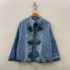 Puede incluir: Chaqueta azul claro con intrincados bordados en tonos verdes y azules. La chaqueta presenta un cuello mandarín y un diseño frontal abierto. El bordado se concentra a lo largo de los bordes delanteros y el dobladillo, agregando un toque decorativo a la prenda.
