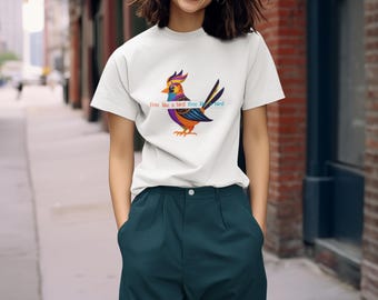Puede incluir: Camiseta blanca con una ilustración de un pájaro colorido y el texto "Free like a bird free". El diseño del pájaro incluye tonos de morado, naranja, azul y amarillo. La persona lleva pantalones verde azulado oscuro.