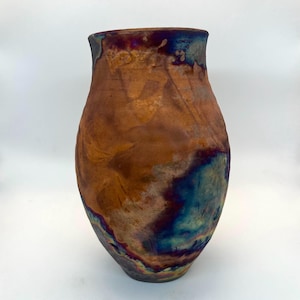 May include: A ceramic vase with a rounded body and a wide opening. The surface features a mottled finish with blended tones of burnt orange, copper, deep blue, and iridescent purple, creating a textured appearance across the entire exterior.