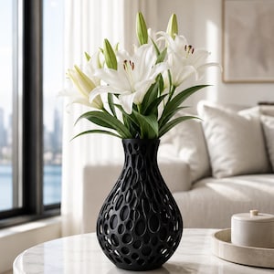 May include: A black, openwork vase filled with white lilies. The vase sits on a marble-topped table, with a cityscape visible through a window in the background. The lilies have green stems and leaves.