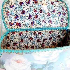 May include: A vintage, blue and white floral patterned box with a turquoise crocheted trim. The inside of the box is lined with a white fabric with a blue and red floral pattern.