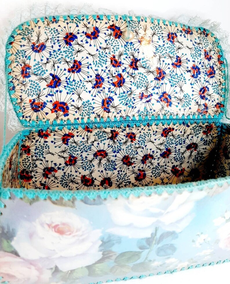 May include: A vintage, blue and white floral patterned box with a turquoise crocheted trim. The inside of the box is lined with a white fabric with a blue and red floral pattern.