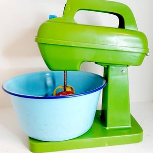 Puede incluir: Un batidor de pie de juguete de plástico verde con un tazón azul y un accesorio de mezcla amarillo, rojo y verde.