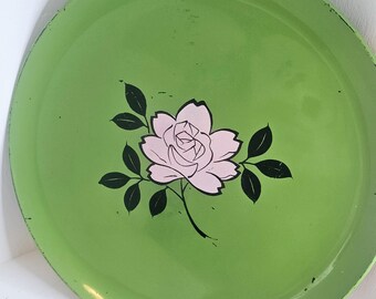 May include: Round, vintage green metal tray with a pink rose and black leaves design. The tray has a slightly worn appearance, adding to its retro charm. A decorative piece for serving or display.