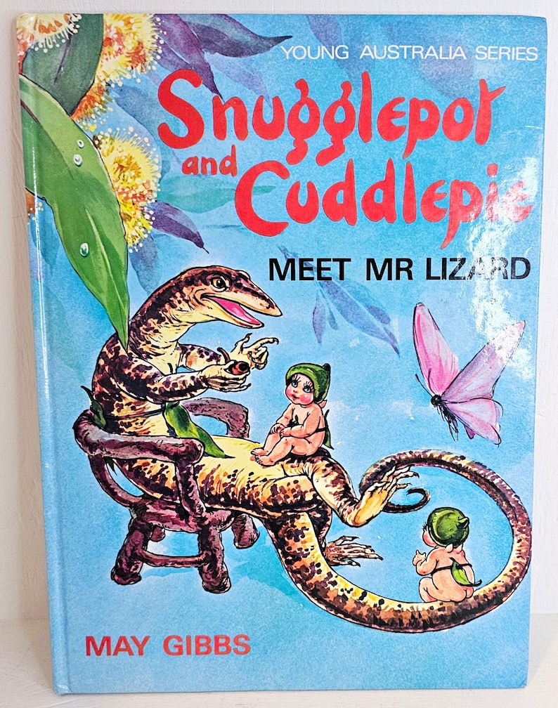 Puede incluir: Una portada de libro infantil con un lagarto de dibujos animados con dos ni&ntilde;os peque&ntilde;os sentados sobre &eacute;l. El t&iacute;tulo del libro es "Snugglepot y Cuddlepie conocen al Sr. Lagarto" y la autora es May Gibbs. La portada es azul con un dise&ntilde;o floral amarillo y verde.