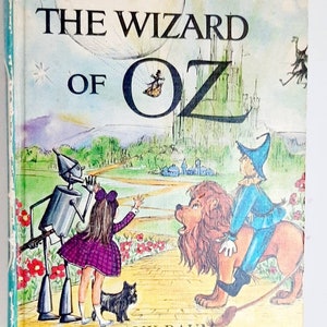 Puede incluir: La portada de un libro infantil titulado "El Mago de Oz" de L. Frank Baum. La portada presenta ilustraciones de Dorothy, el Espantapájaros, el Hombre de Hojalata y el León Cobarde. Las ilustraciones están en un estilo de dibujos animados colorido.