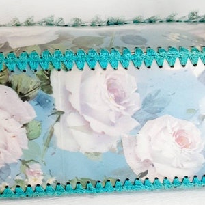 May include: A turquoise blue crocheted trim surrounds a light blue background with a floral pattern of white roses.