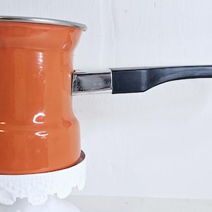 May include: Orange enamel coffee pot with a black plastic handle and a white ceramic base.