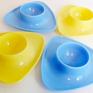 May include: Four triangular egg cups, two blue and two yellow, with a smooth, glossy finish.