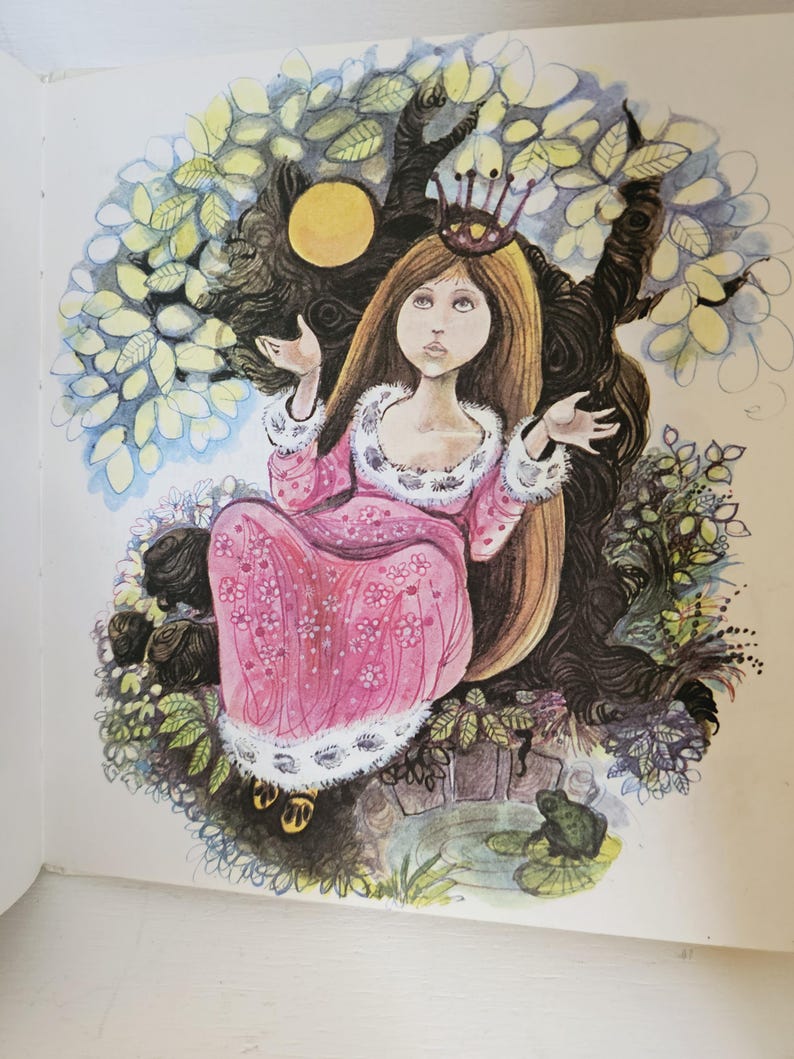 Puede incluir: Ilustraci&oacute;n de una princesa con largo cabello casta&ntilde;o, vestida con un vestido rosa con ribetes blancos y una corona. Est&aacute; sentada en un &aacute;rbol con tronco y ramas oscuras, rodeada de hojas y un estanque con una rana.