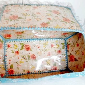 Pu&ograve; includere: Una scatola di tessuto blu chiaro con un motivo floreale e un coperchio di plastica trasparente. La scatola &egrave; foderata con un tessuto bianco con un motivo floreale e ha un bordo in crochet blu.