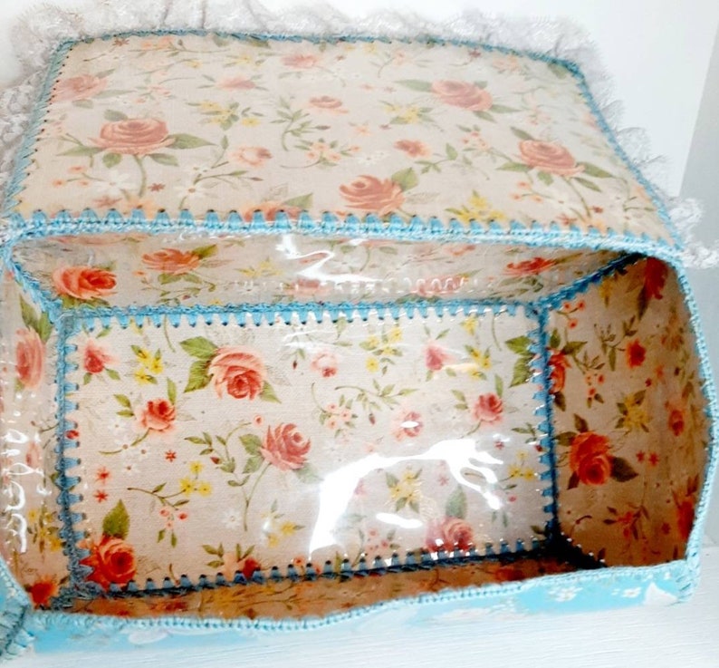 Pu&ograve; includere: Una scatola di tessuto blu chiaro con un motivo floreale e un coperchio di plastica trasparente. La scatola &egrave; foderata con un tessuto bianco con un motivo floreale e ha un bordo in crochet blu.