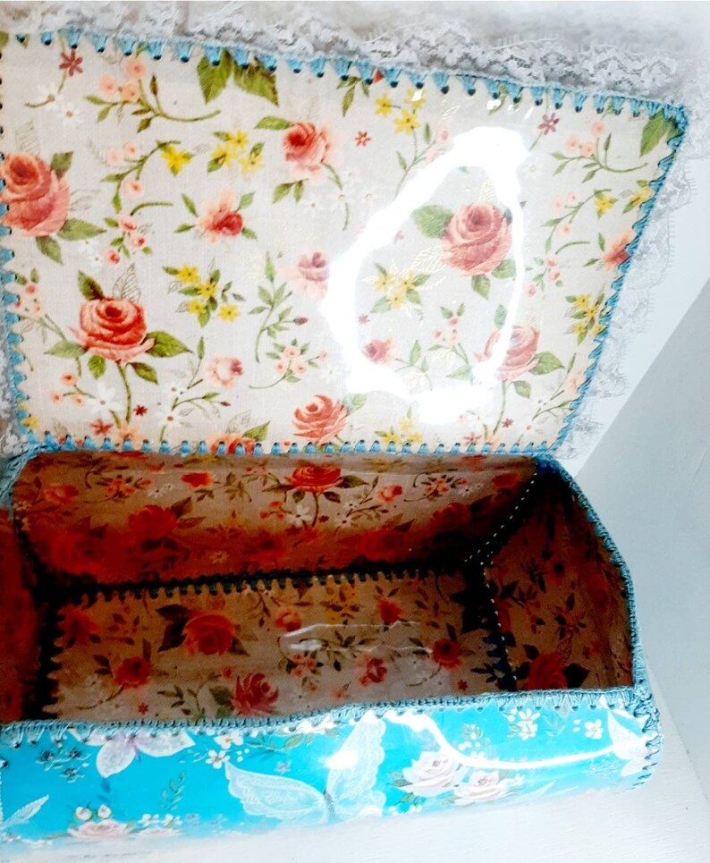 Pu&ograve; includere: Una scatola turchese con un motivo floreale e un design a farfalla. La scatola &egrave; aperta e l'interno &egrave; rivestito con un tessuto floreale.