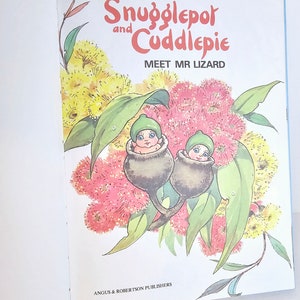 Puede incluir: Una portada de libro con dos peque&ntilde;as hadas con gorros verdes anidadas en nueces de goma. El t&iacute;tulo del libro es "Snugglepot and Cuddlepie Meet Mr Lizard" con un fondo de flores rosas y amarillas.