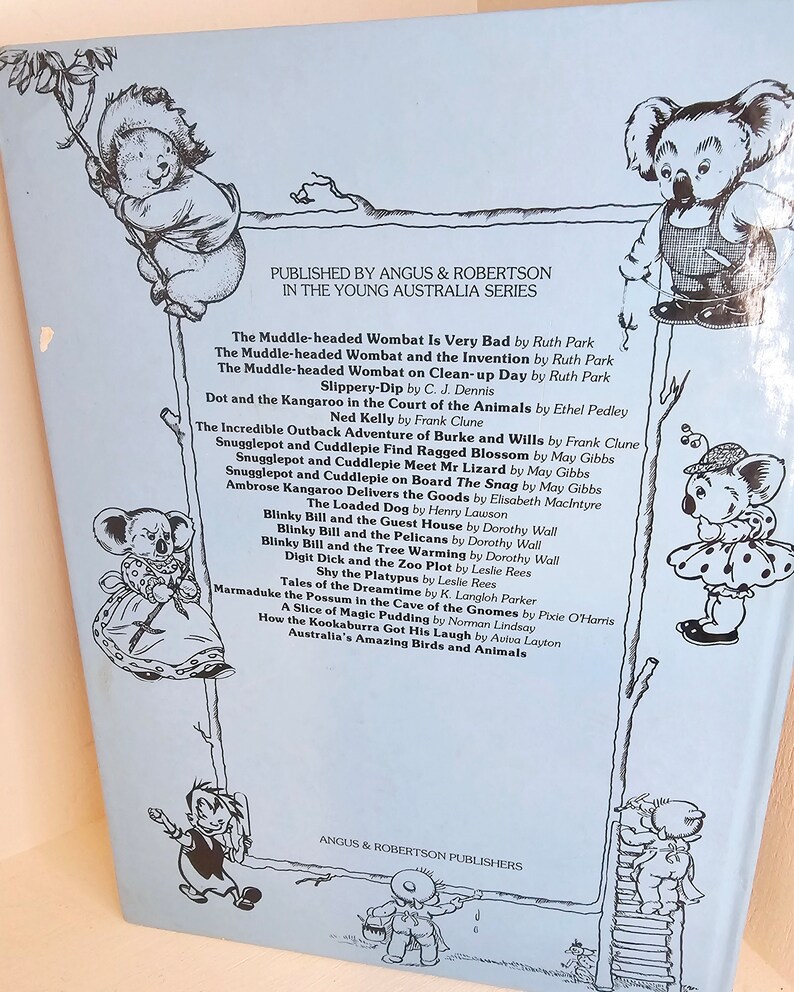 Puede incluir: Una cubierta de libro azul con una lista de libros infantiles publicados por Angus & Robertson. La cubierta presenta ilustraciones de un koala y un wombat.